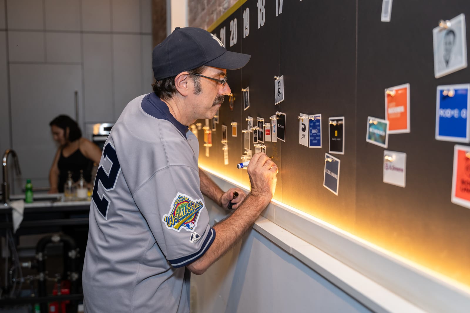 A guest in a Yankees cap and jersey adds a note to the timeline wall with a marker