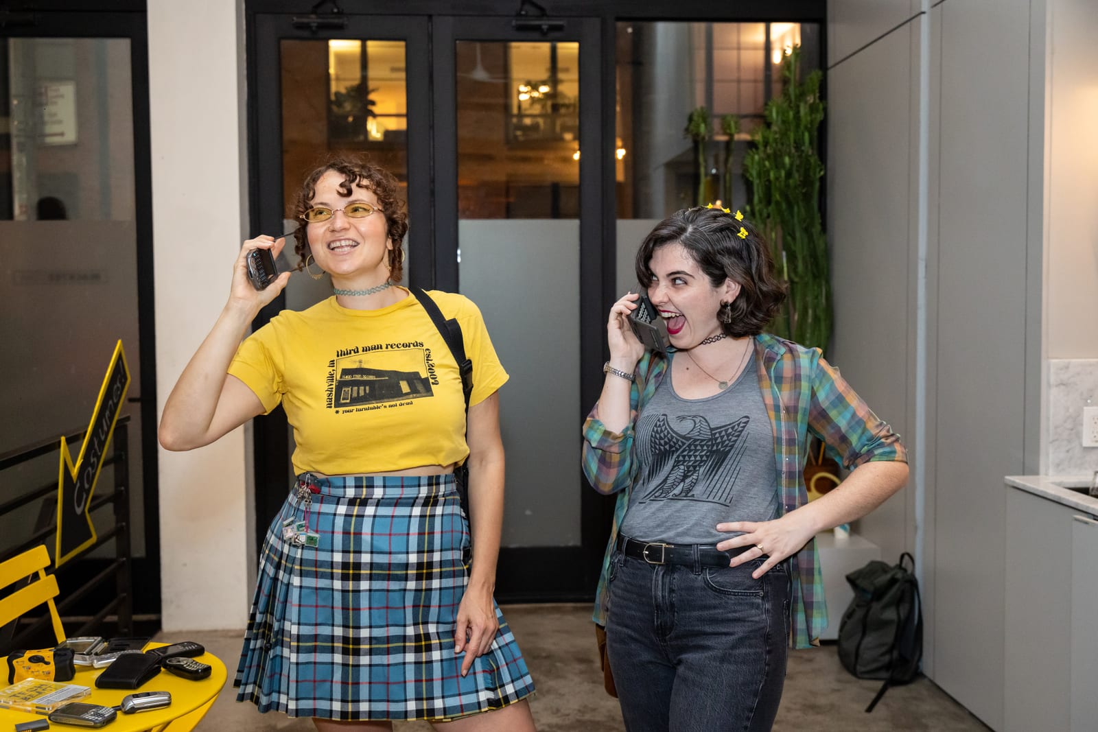 Two guests laugh while holding vintage cell phones up to their ears at a table set with more retro phones