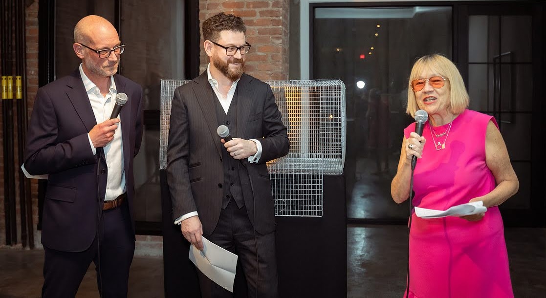 Michael Horst, Noah Landow, and Cindy Gallop speaking with microphones in front of the wire cage installation