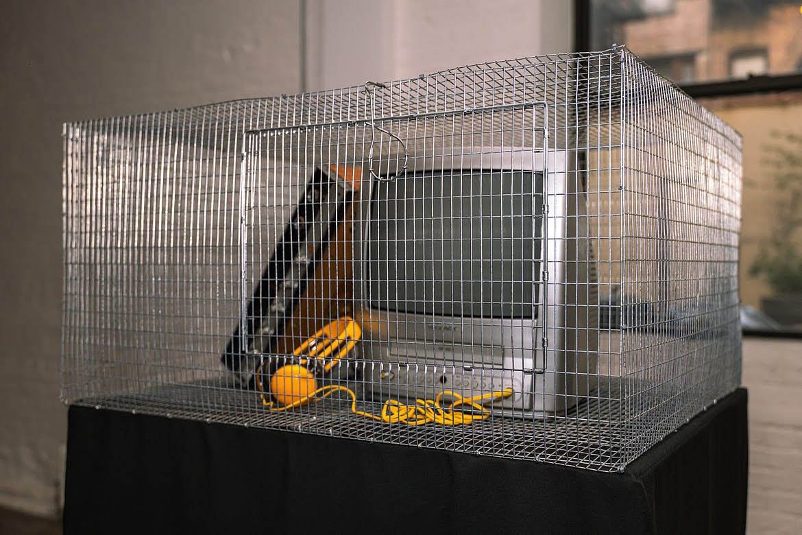 Wire cage containing an old CRT monitor and yellow cables, part of the tech beast installation