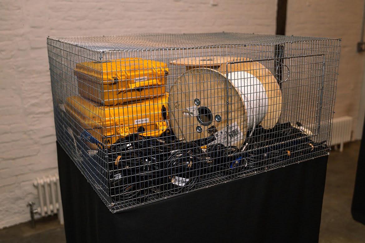 Wire cage containing yellow equipment cases, a cable reel, and tangled cables