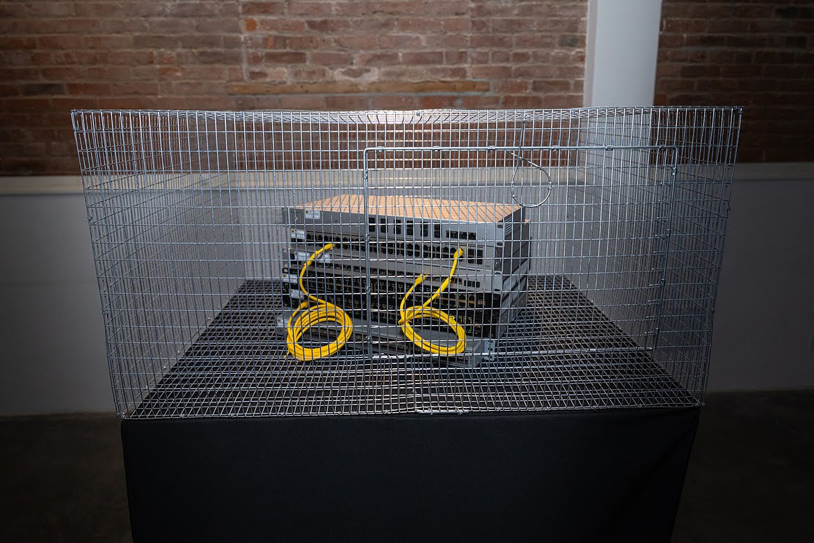 Wire cage containing stacked network switches and coiled yellow ethernet cables