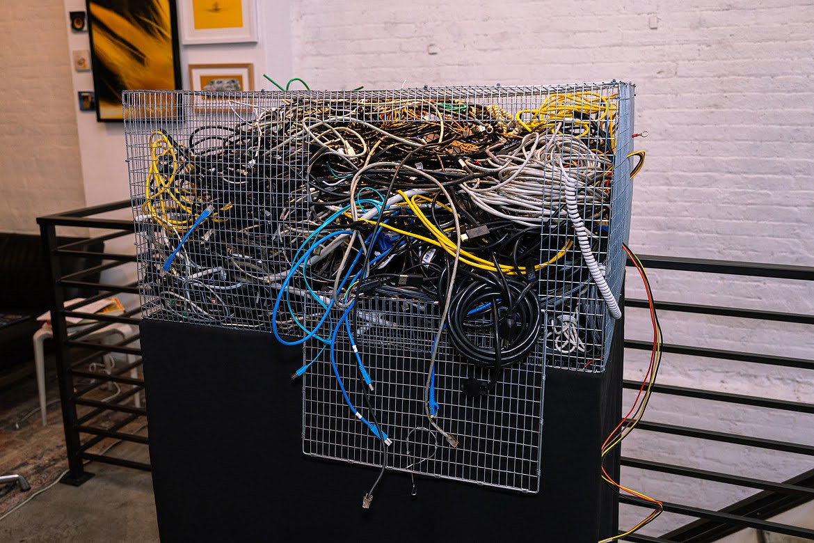 Wire cage overflowing with a tangle of multicolored network and power cables
