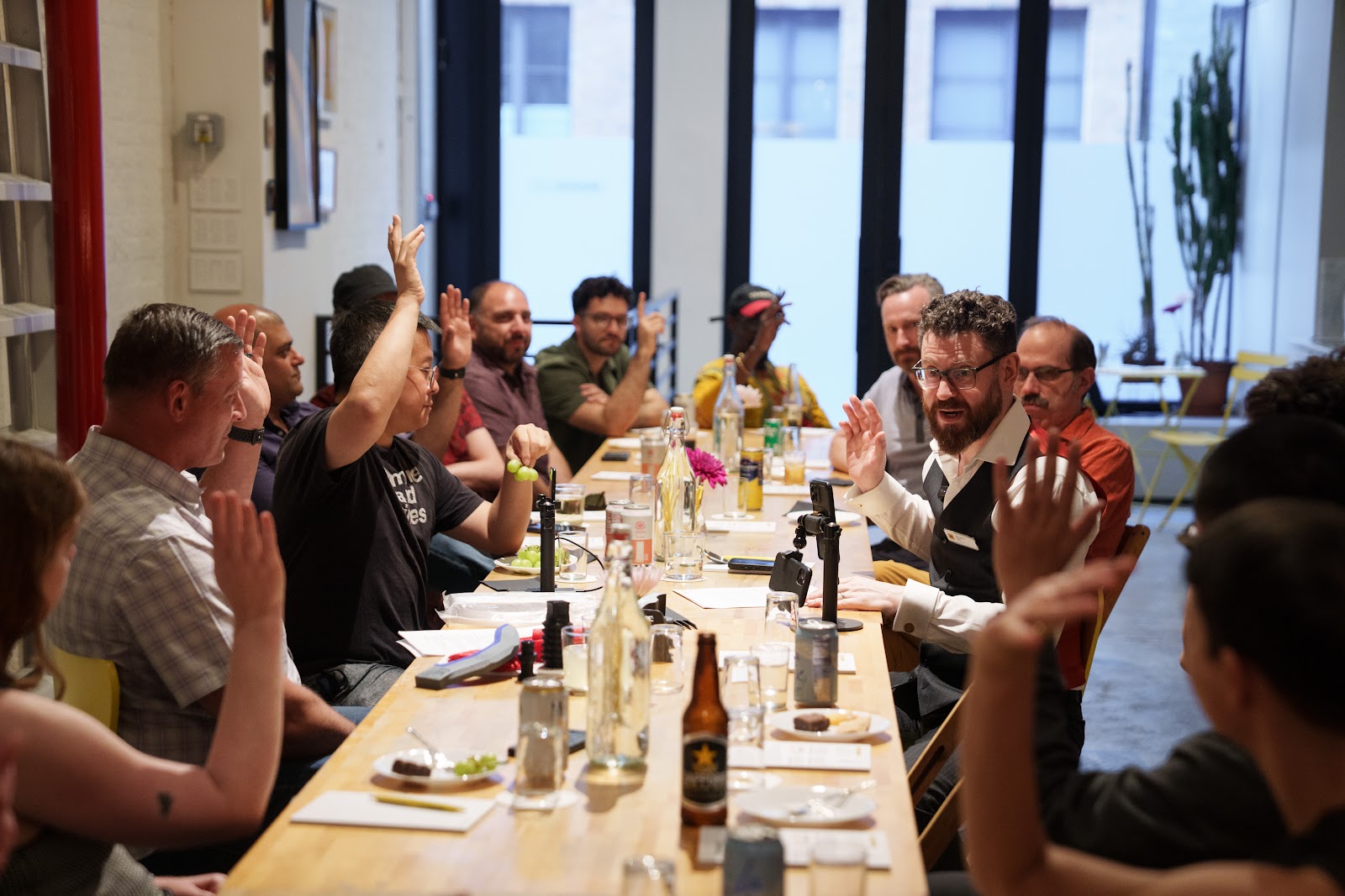 Attendees seated around the long table during the Modern Alchemy Tête-à-Tech, several with hands raised